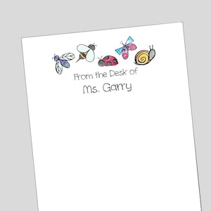 May include: White notepad with a line of colorful cartoon insects, including a bee, ladybug, butterfly, and snail. The text "From the Desk of Ms. Garry" is printed below the insects.