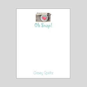 May include: A white notepad with a watercolor illustration of a vintage camera with a red heart in the viewfinder. The text "Oh Snap!" is written in teal blue below the camera. The name "Casey Speltz" is written in teal blue at the bottom of the notepad.