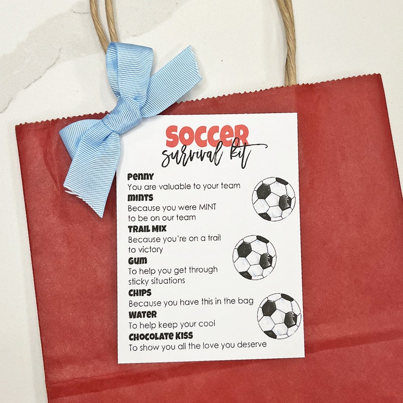 May include: A white card with the text "Soccer Survival Kit" in red and black lettering. The card lists items with a soccer ball icon next to each item. The items are: Penny, Mints, Trail Mix, Gum, Chips, Water, and Chocolate Kiss.