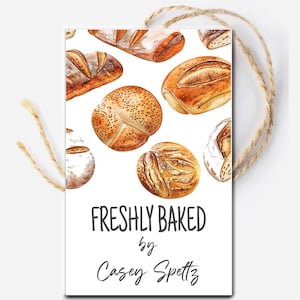 Könnte beinhalten: Ein weißes Etikett mit einer Aquarellillustration verschiedener frisch gebackener Brote und Brötchen. Der Text "FRESHLY BAKED by Casey Spettz" ist in schwarzer Schrift geschrieben. Eine natürliche Schnurschlaufe ist befestigt.