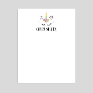 May include: A white unicorn face with a rainbow horn and colorful flowers on its head. The unicorn has closed eyes and a pink nose. The text "Casey Speltz" is below the unicorn.