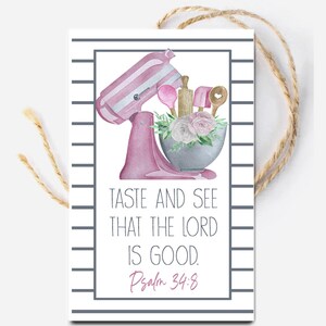 May include: A rectangular gift tag with a striped border and jute twine, featuring a watercolor illustration of a pink stand mixer, a grey mixing bowl filled with pink roses, and kitchen utensils. Text reads: TASTE AND SEE THAT THE LORD IS GOOD. Psalm 34:8.
