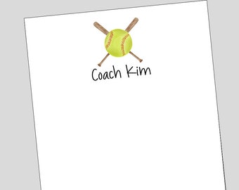 May include: A white notepad with a yellow softball and two crossed wooden bats. The text "Coach Kim" is written below the softball.
