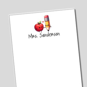 May include: A white notepad with a red apple and a yellow pencil with a smiling face. The text "Mrs. Sanderson" is written on the notepad.