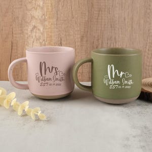May include: Two ceramic mugs, one pink and one green, with matching handles and speckled finish. The pink mug says "Mrs. William Smith EST 05.19.2025" and the green mug says "Mr. William Smith EST 05.19.2025".