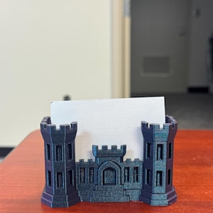 May include: A black and green 3D printed business card holder shaped like a castle.