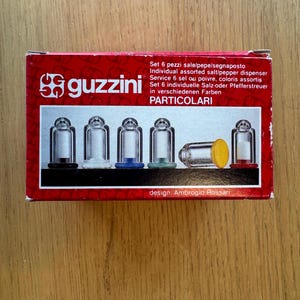 Peut inclure: Une boîte rouge avec la marque "guzzini" et du texte en plusieurs langues. La boîte contient six salières et poivrières individuelles de différentes couleurs. Le design est d'Ambrogio Rossari.