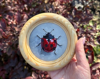 May include: A small wooden frame with a painted image of a ladybug on a gray background.