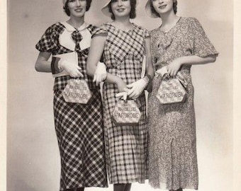 Puede incluir: Tres personas con vestidos de largo medio, sombreros y guantes, cada una sosteniendo un bolso pequeño con la etiqueta "Randelle Wardrobe". Los vestidos tienen estampados de cuadros y flores. Llevan sandalias de tacón sobre una plataforma.