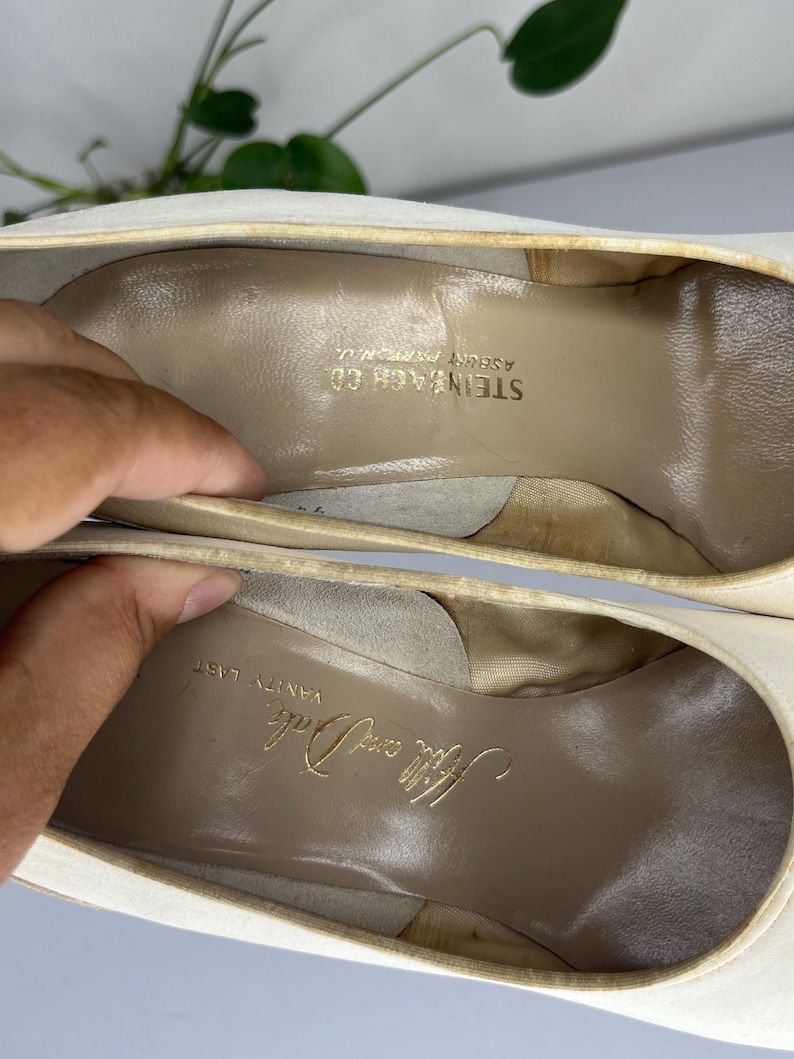 May include: Close-up of the inside of a pair of off-white high heels. The insoles are tan with gold lettering that reads "Hilly and Dale" and "Steinbach Co Asbury Park N.J."
