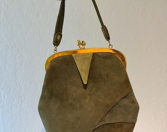 May include: Olive green suede handbag with a geometric design. The bag has a gold-toned clasp and trim, and a matching green handle. The bag is held up by a hand.