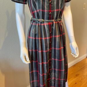 Peut inclure: Robe &agrave; carreaux grise, rouge et noire, &agrave; manches courtes et &agrave; boutons sur le devant. La robe est cintr&eacute;e &agrave; la taille par une fine ceinture. La robe est pr&eacute;sent&eacute;e sur un mannequin.