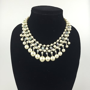 May include: A multi-layered pearl necklace with crystal accents. The necklace features a cascading design with large pearls and smaller crystals.