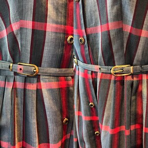 Peut inclure: Gros plan de deux robes &agrave; motif &agrave; carreaux gris, rouges et noirs. Chaque robe a une ceinture assortie avec une boucle dor&eacute;e. Les robes ont un devant boutonn&eacute; et des manches courtes. Les robes sont probablement de style vintage ou r&eacute;tro.