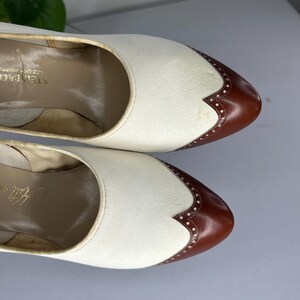 May include: Pair of vintage women's shoes. The shoes are two-tone, with white uppers and brown leather toe caps. The toe caps have decorative perforations. The shoes are in good condition, with some signs of wear. The brand name "Steinbach" is visible inside the shoe.