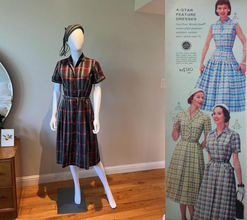 Peut inclure: Une robe &agrave; carreaux de style vintage en gris, rouge et noir, pr&eacute;sent&eacute;e sur un mannequin. La robe pr&eacute;sente des manches courtes, une fermeture boutonn&eacute;e sur le devant et une ceinture assortie. Un chapeau assorti est &eacute;galement sur le mannequin. Une publicit&eacute; vintage pour des robes est en arri&egrave;re-plan.
