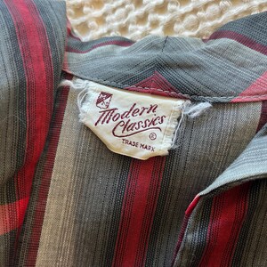 Peut inclure: Gros plan sur une chemise vintage &agrave; rayures grises, rouges et noires. La chemise pr&eacute;sente un col et une &eacute;tiquette indiquant "Modern Classics TRADE MARK". Le tissu a un aspect doux et textur&eacute;.