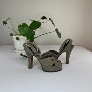 May include: A pair of vintage sage green platform heels. The open-toe shoes have a cut-out design on the vamp and a strap that wraps around the ankle. The heels are approximately 4 inches tall.