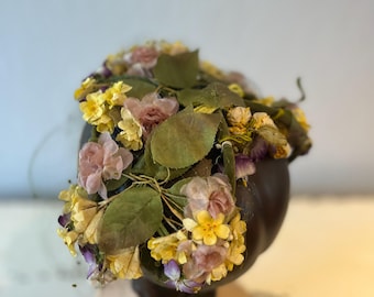 Puede incluir: Un tocado floral con flores rosas, amarillas y moradas y hojas verdes.