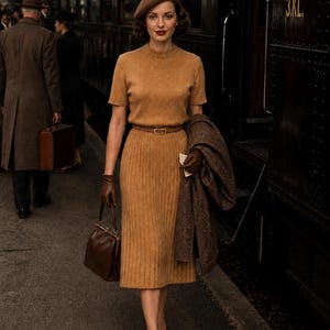 Peut inclure: Un haut à manches courtes en tricot beige et une jupe midi côtelée assortie avec une fine ceinture marron, un béret marron, des gants en cuir marron, un sac à main marron et un manteau à motifs marron et noir sur le bras, près d'un train.