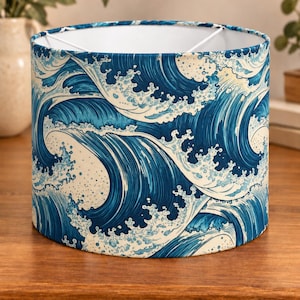 Op de afbeelding: Een cilindrische trommellampenkap met een herhalend patroon van gestileerde blauwe en witte oceaangolven. Het ontwerp toont diepblauw water met witte schuimkoppen en gedetailleerde lijnen op een crèmekleurige achtergrond.
