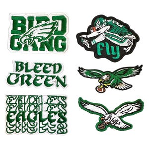 May include: A collection of green and white embroidered patches. The patches feature text like "BIRD GANG", "BLEED GREEN", and "EAGLES". Other patches depict an eagle and a football player.