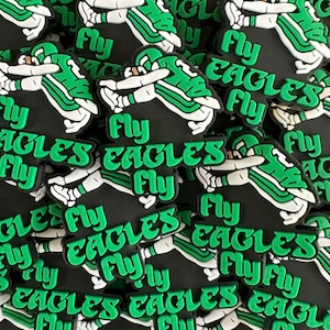 May include: A close-up of a pile of green and black rubber charms with the words "Fly Eagles Fly" printed on them. The charms are shaped like a football player in a green and white uniform.