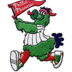 May include: Embroidered patch featuring the Philadelphia Phillies mascot, the Phillie Phanatic. The green, furry creature is running and holding a red banner that reads "Phillie Phanatic". The patch has a white border.