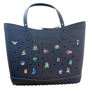 K&ouml;nnte beinhalten: Eine schwarze Tragetasche mit Griff und dekorativen Anh&auml;ngern. Die Tasche hat ein perforiertes Design und einen strukturierten Boden. Die Anh&auml;nger sind farbenfroh und zeigen verschiedene Sportmotive.