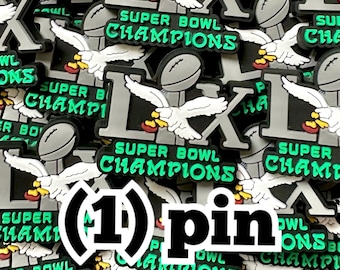 以下が含まれることがあります： 緑と白で「SUPER BOWL CHAMPIONS」の文字が入ったピンのコレクション。ピンにはフットボール、ローマ数字の「LIX」、白いワシが描かれています。「pin」の文字も確認できます。