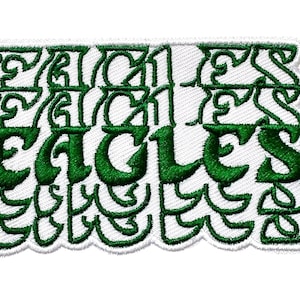 May include: A rectangular white embroidered patch with the word "EAGLES" in large, green, stylized letters. The patch has a scalloped edge and additional green decorative elements above the word.