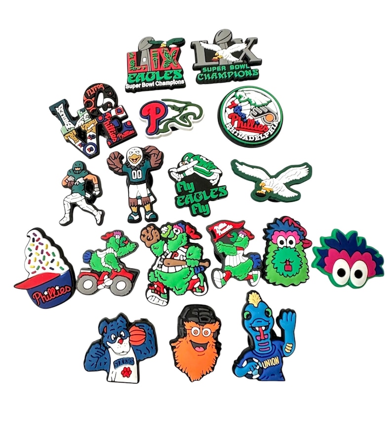 K&ouml;nnte beinhalten: Eine Sammlung bunter Schuhanh&auml;nger mit Logos und Maskottchen von Philadelphia-Sportteams. Zu den Anh&auml;ngern geh&ouml;ren die Eagles, Phillies und verschiedene Teammaskottchen. Die Anh&auml;nger sind aus Gummi und haben ein 3D-Design.