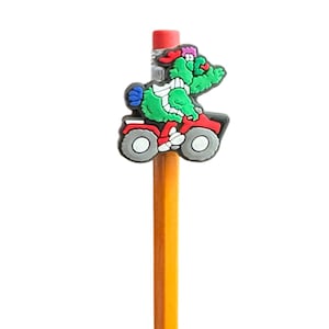 Puede incluir: Un l&aacute;piz amarillo con un personaje de dibujos animados verde montando un quad rojo. El personaje lleva un sombrero rojo. El l&aacute;piz tiene una goma de borrar roja y est&aacute; sobre un fondo blanco.