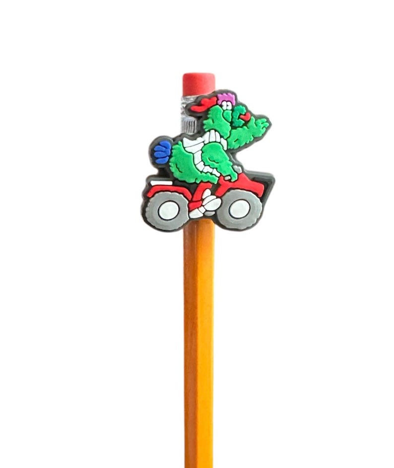 Puede incluir: Un l&aacute;piz amarillo con un personaje de dibujos animados verde montando un quad rojo. El personaje lleva un sombrero rojo. El l&aacute;piz tiene una goma de borrar roja y est&aacute; sobre un fondo blanco.