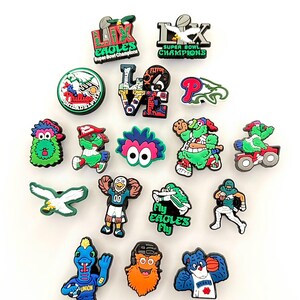 May include: A collection of 17 colorful shoe charms featuring the Philadelphia Eagles logo, mascot, and other team-related imagery. The charms include the words "Fly Eagles Fly", "Super Bowl Champions", and "Love".