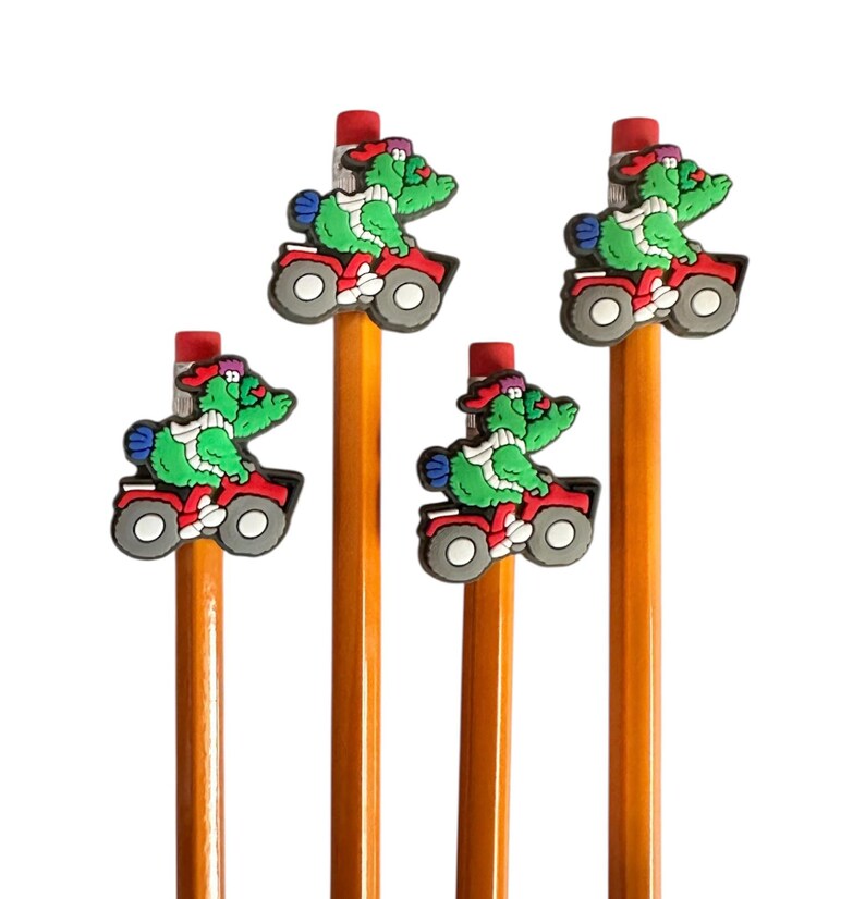 Puede incluir: Cuatro l&aacute;pices con gomas de borrar rojas y adornos de cocodrilo de dibujos animados montados en quads rojos. Los cocodrilos son verdes con bufandas blancas y sombreros rojos. Los l&aacute;pices son amarillos.