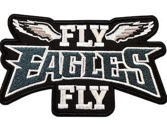 May include: An embroidered fabric patch featuring the text FLY EAGLES FLY in white and dark teal lettering. The design includes a pair of white wings above the word FLY and is outlined in black thread against a solid black background.