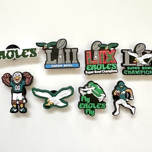 May include: A set of eight Philadelphia Eagles themed shoe charms in various shapes and designs, including the team name, Super Bowl LII and LIX logos, a mascot, a flying eagle, and a football player, all rendered in green, white, black, and silver.