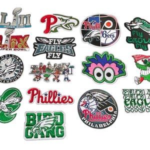 May include: A collection of embroidered patches featuring logos and text related to Philadelphia sports teams. Designs include the Eagles, Phillies, and Super Bowl imagery, with various colors and styles.