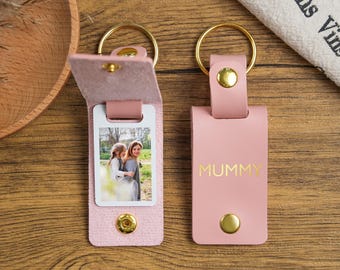 Pode incluir: Chaveiro de couro rosa com um inserto para fotos e uma inscrição dourada que diz "MUMMY".
