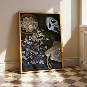 May include: A framed image with a horror movie theme. It features a Scream mask, popcorn in a wooden bowl, a vintage telephone, and Polaroid photos with horror movie images. The background is black.