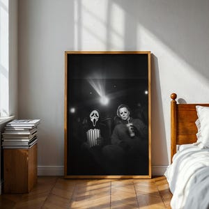 May include: Black and white framed print featuring two iconic horror movie characters in a movie theater setting. One holds popcorn, the other a drink. The image is illuminated by the projector's light.