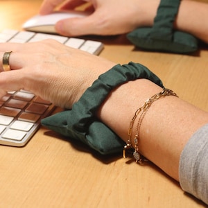 May include: Dark green wrist supports for keyboard use. The supports are made of a soft fabric and are designed to support the wrists while typing. The image shows a person using a computer with the supports in place.