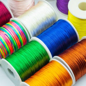May include: A selection of colourful thread spools, featuring pink, white, blue, green, yellow, orange, and purple hues. The thread is neatly wound on white plastic spools, displaying a spectrum of vivid colours.