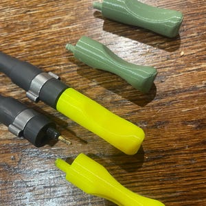 May include: An assortment of fishing rod components, including black and silver rod sections, and bright yellow and green rod handles. The handles are curved and appear to be 3D-printed. The components are arranged on a wooden surface.