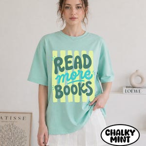 Puede incluir: Camiseta verde menta con las palabras "READ more BOOKS" en una fuente juguetona. El texto est&aacute; sobre un fondo de rayas verticales amarillas. La camiseta forma parte de la colecci&oacute;n "Chalky Mint".