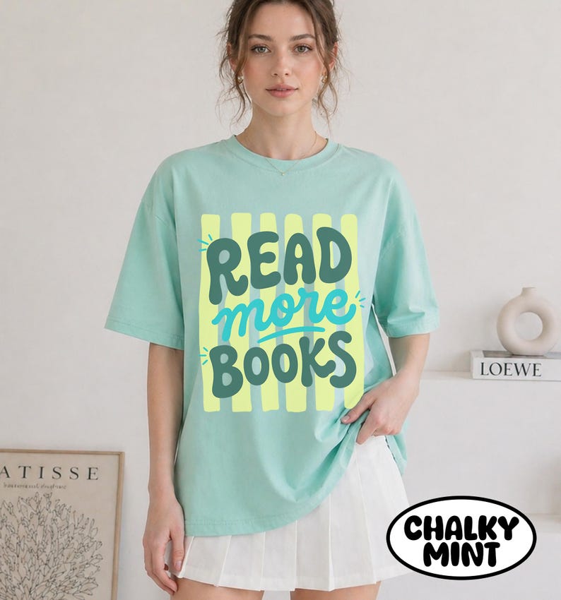 Puede incluir: Camiseta verde menta con las palabras "READ more BOOKS" en una fuente juguetona. El texto est&aacute; sobre un fondo de rayas verticales amarillas. La camiseta forma parte de la colecci&oacute;n "Chalky Mint".