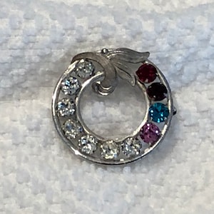 May include: A silver ring with a swirl design and a row of colorful gemstones. The gemstones are red, purple, blue, and green.