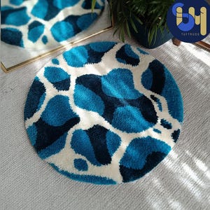 May include: A round, white and blue rug with a blue and black abstract pattern. The rug is made of fluffy, tufted yarn.