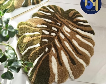 May include: A round, green, brown, and white rug with a large leaf design. The rug is made of tufted yarn and has a soft, plush texture.